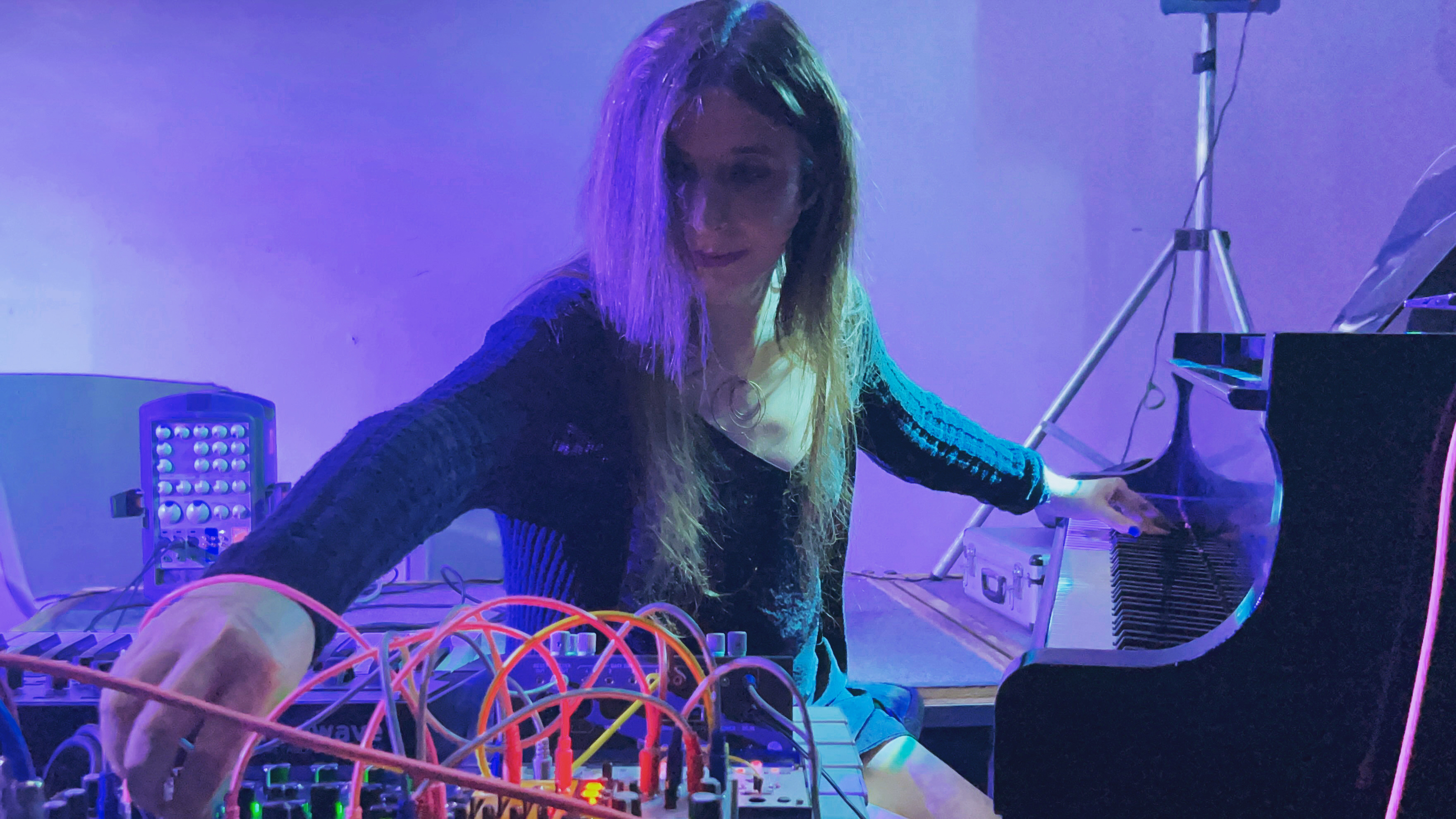 Amanda Chaudhary playing a modular synthesizer next to a grand piano